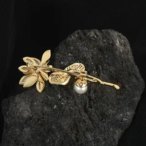 Vue macro de la broche fleur dorée montrant le travail du métal et le pendentif perle