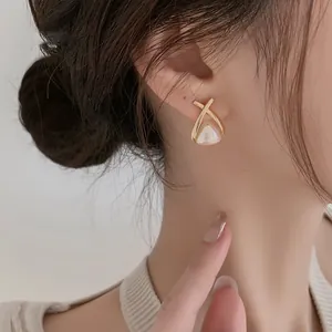 Elegante gouden oorbellen met parel hanger en gekruiste lijnen gedragen door een model