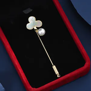 Close-up of golden clover brooch with white shell inlay and pearl in a red jewelry box
