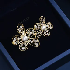 Détail d'une élégante broche florale dorée avec perles blanches et zircons dans un écrin bleu