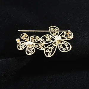 Broche fleur dorée élégante au design évidé et cristaux blancs sur velours noir