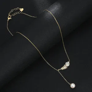 Détail du pendentif plume dorée avec zircon et perle sur une chaîne à pampilles