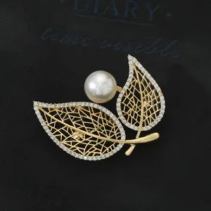 Macro view of gold-plated leaf brooch featuring micro-set cubic zirconia and a large pearl