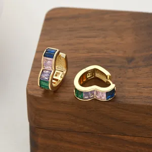 Primer plano de pendientes de corazón dorados con circonitas de colores corte baguette