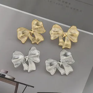 Primer plano de pendientes de lazo de metal cepillado oro y plata con detalle de corazón