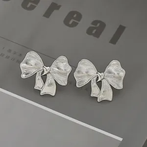 Pendientes de lazo plateados con textura cepillada sobre fondo elegante de revista