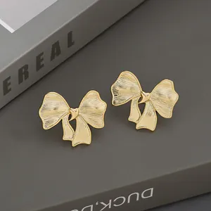 Elegantes pendientes de lazo dorado con textura cepillada y detalle de corazón sobre libro