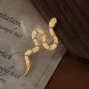 Elegant gold-plated snake brooch with white zircons and green gemstone eyes on vintage paper