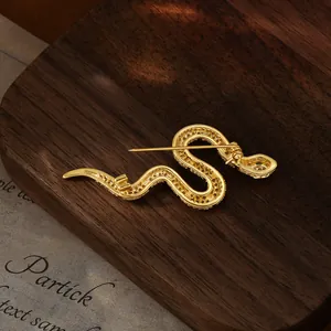Elegant gold-plated snake brooch with sparkling cubic zirconia on a walnut wood base