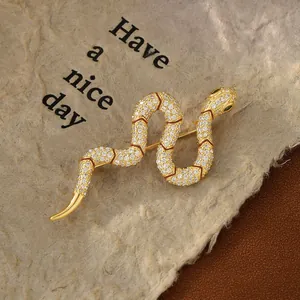Detailed close-up of gold snake brooch with white zircons and green gemstone eyes