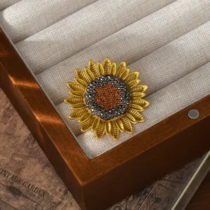 Elegant gold plated sunflower brooch featuring orange and black crystals on a display tray