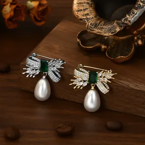 Detailed view of elegant bow brooches with emerald stone and drop pearl on wood background