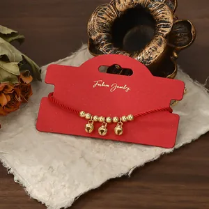 Dettaglio del bracciale a corda intrecciata rossa con campanelli dorati e perline oro