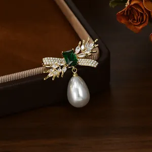 Macro shot of gold wheat brooch with emerald stone and dangling teardrop pearl