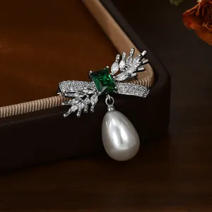 Detail of emerald cut green gem brooch with wheat leaf pattern and drop pearl pendant