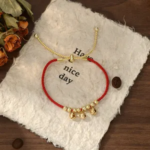 Bracciale a corda rossa intrecciata con campanelli e perline dorate su carta ruvida