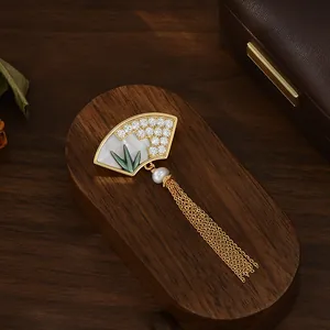 Détail d'une broche en forme d'éventail avec perle, feuilles de bambou et pompons dorés