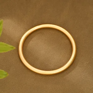 Dettaglio del bracciale dorato con texture opaca e design rotondo su superficie marrone