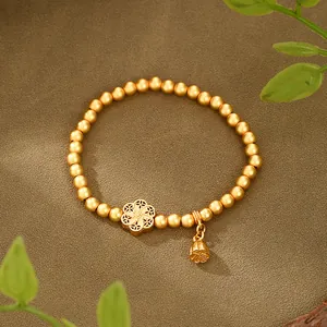 Dettaglio di bracciale in oro opaco con ciondolo a fiore traforato e campanello Fu