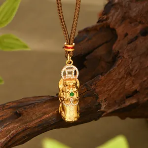Detalle macro del colgante PiXiu dorado con gema verde y diamantes sobre fondo madera