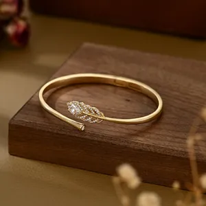 Detail of 14k gold plated feather bangle with pavé zircons on dark wooden background
