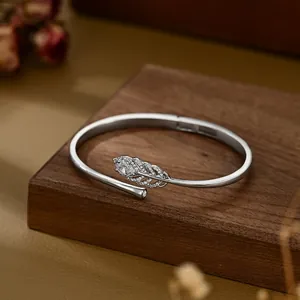 Silver feather cuff bracelet with pavé-set zircons and a pear-cut stone on a wooden base