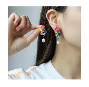 Close-up of a model wearing colorful enamel flower earrings with white pearl pendants