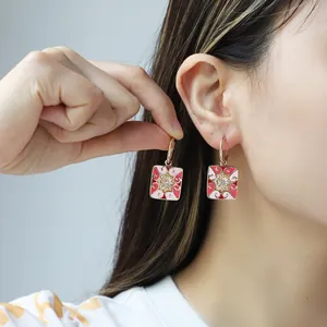 Golden enamel heart earrings with central zircon crystals worn by a model