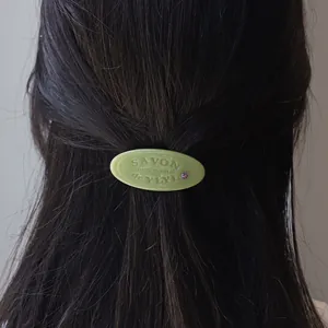 Groene ovale hars haarclip met gegraveerde tekst en strassteen op donker haar