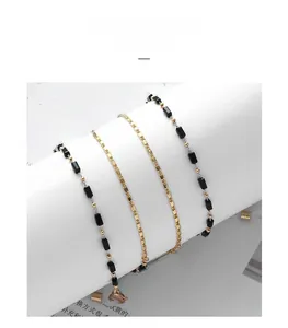 Close-up of three layered necklace chains with gold rope and black crystal accents