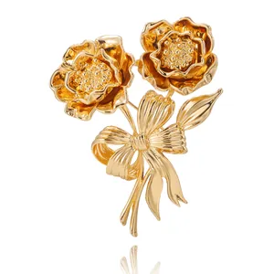 Elegante spilla a fiore dorata con doppi fiori di camelia e un fiocco in metallo lucido
