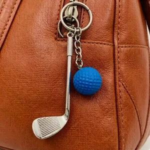 Silver golf club and blue golf ball keychain accessory hanging on a brown leather bag