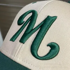 Detail of green 3D embroidered M letter on a beige and green cotton baseball cap