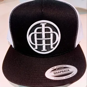 Close-up of embroidered white logo on black panel with white mesh back and silver sticker