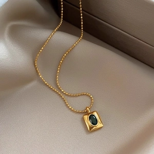 Elegant gold necklace with emerald-green oval gemstone pendant on champagne silk fabric