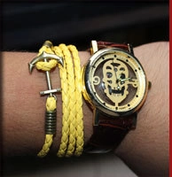 Close-up of gold skull quartz watch with red leather strap and yellow anchor bracelet