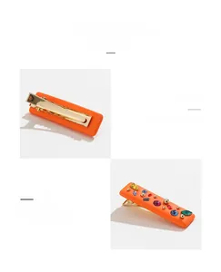 Detail view of orange rectangular hair clip with colorful resin rhinestones and gold duckbill clip