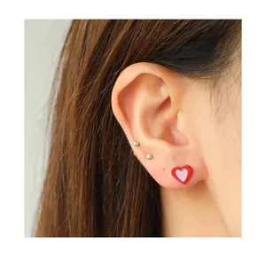 Macro shot of colorful heart-shaped enamel studs and silver ball earrings on model