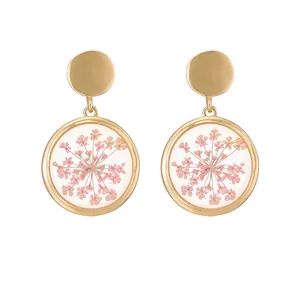 Close-up of golden round earrings with embedded pink dried flowers in clear resin