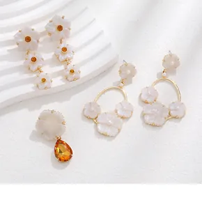 Détail de boucles d'oreilles fleurs en résine avec monture dorée et cristaux oranges