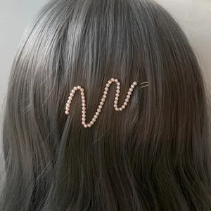 Elegant gold wavy hair clip with white pearls worn on dark hair, stylish hair accessory