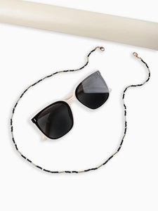 Detail of black and gold beaded eyewear chain with white sunglasses on white background