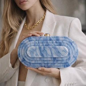 Detail view of marble patterned acrylic evening bag with gold clasp held by a model