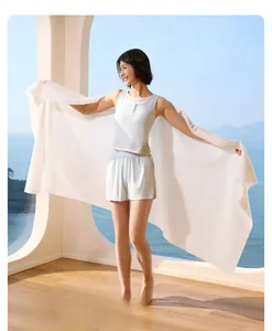 Extra-large white disposable bath towel for travel shown by model in front of sea view