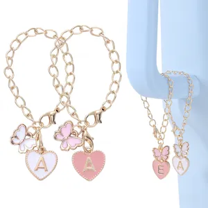 Detail of a gold letter heart and pink butterfly charm on a delicate chain accessory