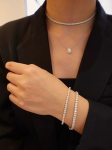 Detailed close-up of sparkling tennis bracelets and pear-cut pendant necklace on model