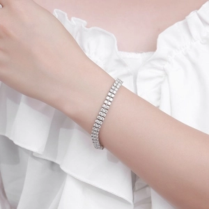 Macro detail of elegant silver double-row tennis bracelet worn on a white textured sleeve