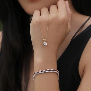 Close-up of sparkling tennis bracelets and a gold solitaire pendant necklace on wrist