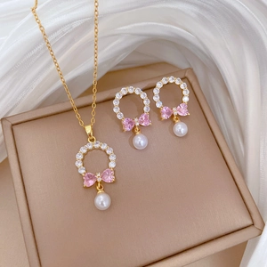 Detail view of gold necklace and earrings set with pink bows and pearls on silk