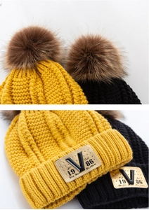 Close-up of thick knit winter hat featuring plush faux fur pompom and metal V-tag logo